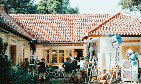 A film crew sets up lights and equipment outside a house for a shoot.