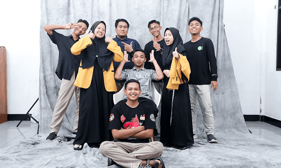 A diverse group of eight young people happily pose for a photo in a studio.