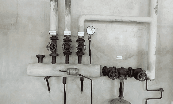 Industrial piping system with multiple valves and a pressure gauge on a concrete wall.