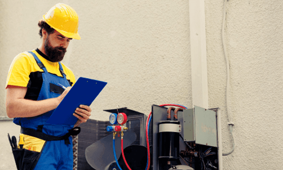A technician in a hard hat inspects an outdoor AC unit, writing notes on a clipboard.